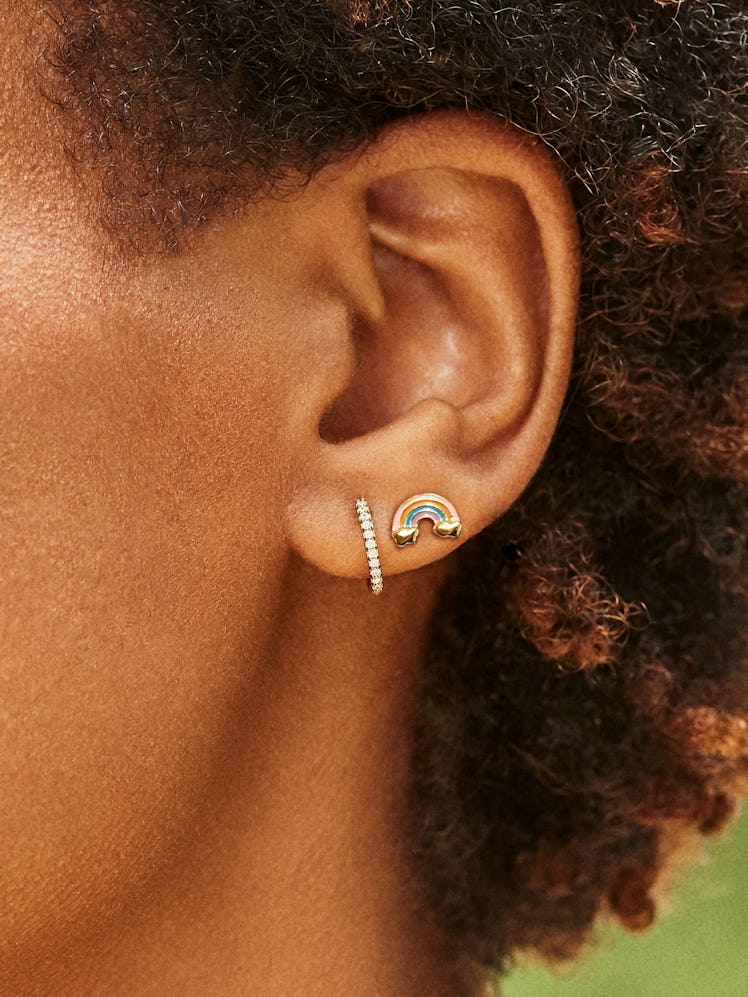 A black model with short, natural hair texture models two dainty pieces of jewelry: a rhinestone hoo...