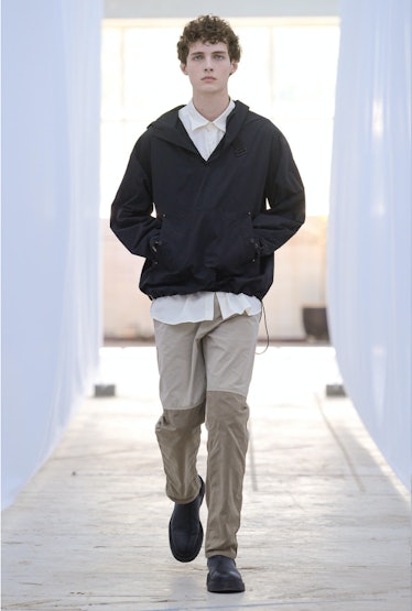 A male model walking in a black jacket and light brown pants by Berner Kühl