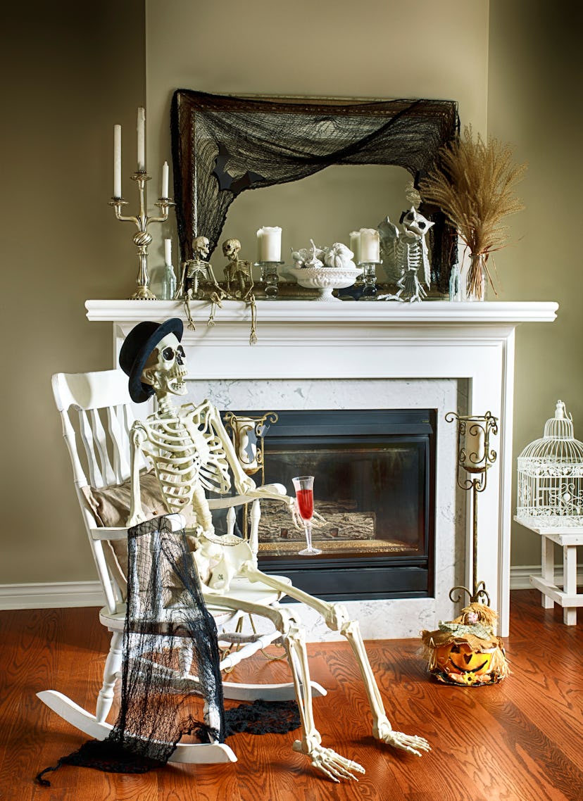 A fireplace decorated in spooky Halloween decor with a skeleton siting in a rocking chair in front o...