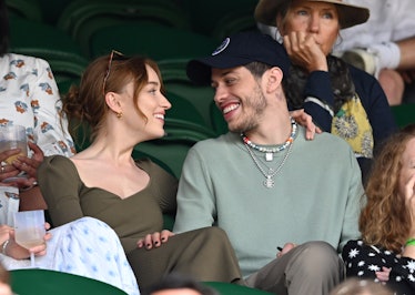 Phoebe Dyneover in a khaki dress and Pete Davidson in a sage sweater and grey pants in the stands at...