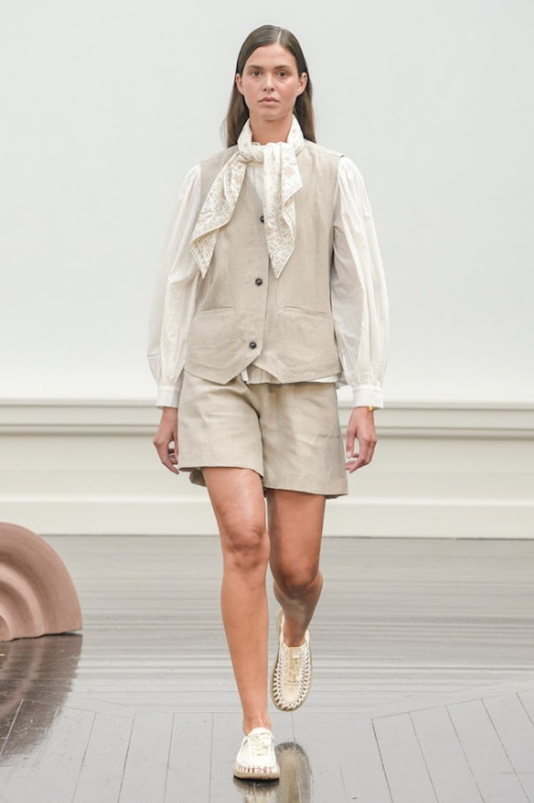 A model walking the runway at Copenhagen Fashion Week in a white shirt, light grey vest and shorts b...