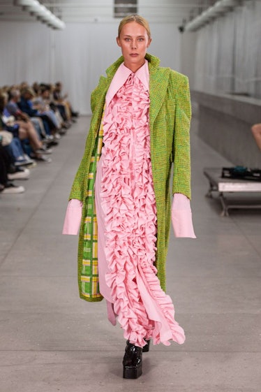 A model in a pink dress with ruffles and a green coat by Frederik Taus 