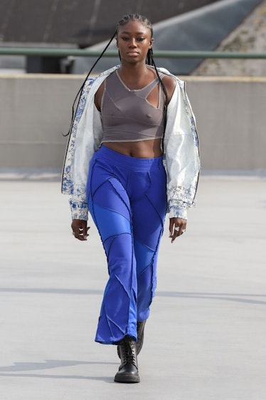 A model walking in a white and blue jacket, grey training bra and blue pants by (Di)vision