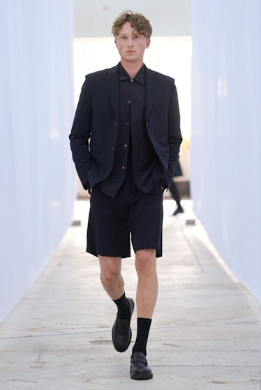 A male model walking in black shorts, blazer, and shirt by Berner Kühl