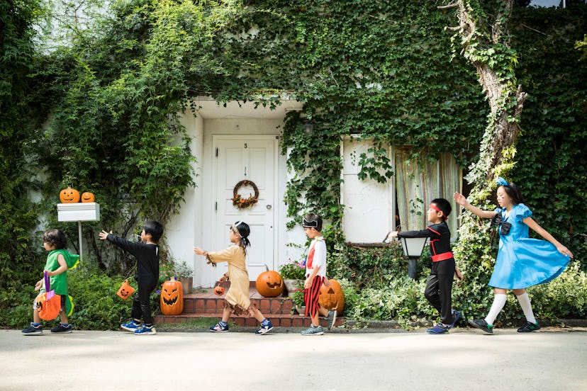 Wide shot of six kids walking in a line, dressed in Halloween costumes