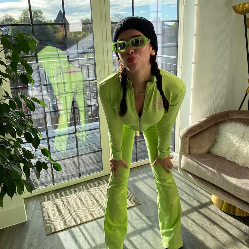Dua Lipa wears a neon orange tracksuit adorned with '90s-style braided pigtails. 