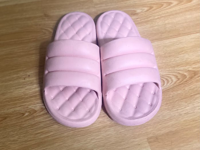 A pair of puffy pink Floppers slippers is shown on a wood floor