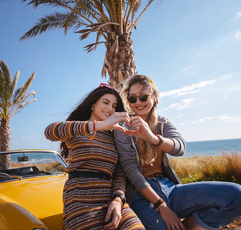 2 friends sitting on a car making a heart with their hands before posting on Instagram with a captio...