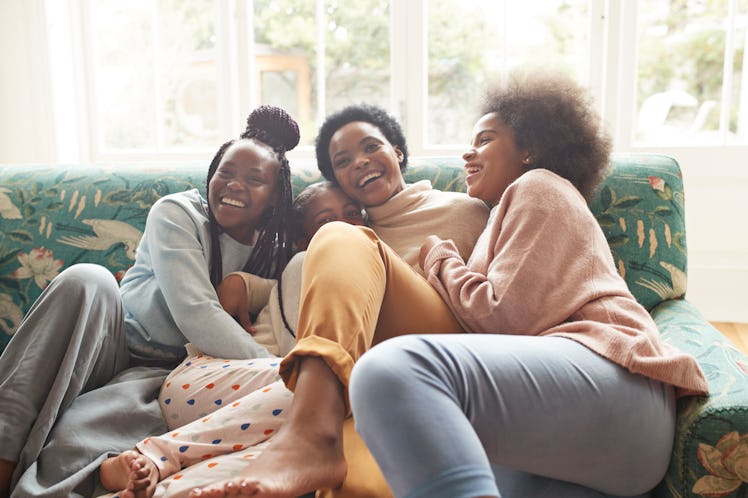 Happy woman with her 3 teen daughters hugging on the couch before posting pic on Instagram with moth...