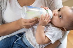 A baby drinking milk from a glass baby bottle
