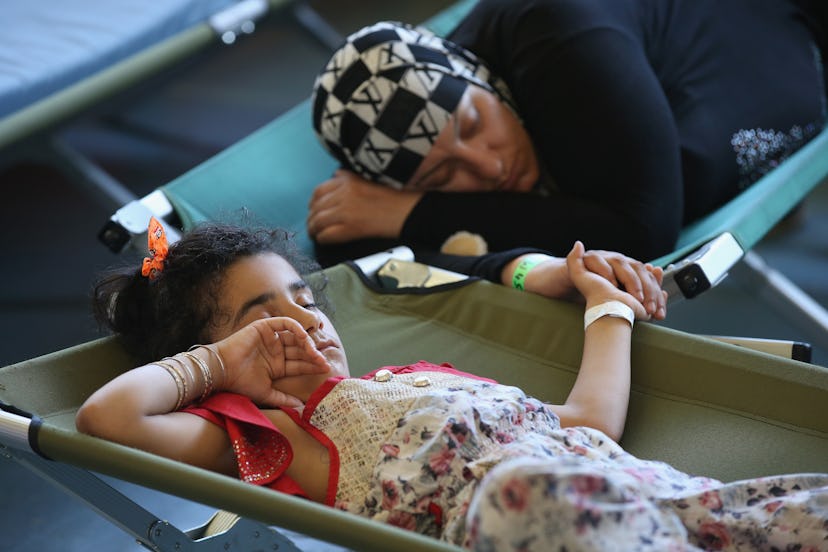 A mother and daughter clutch hands as they sleep on cots at a registration center for migrants at a ...