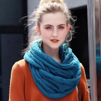 A blue, knitted infinity scarf being worn with an orange sweater.