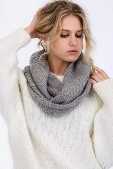 A woman wearing a gray infinity scarf and white sweater.