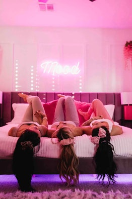 Friends relax on a bed in a 'Love Island'-themed Airbnb with neon lights in the bedroom. 