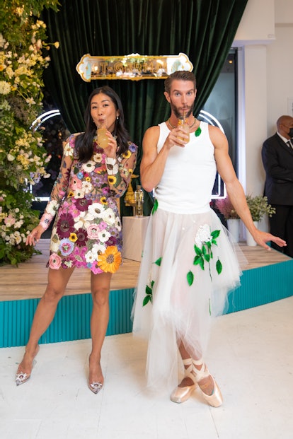 Laura Kim in a floral dress sipping a drink next to a man dressed as a ballerina