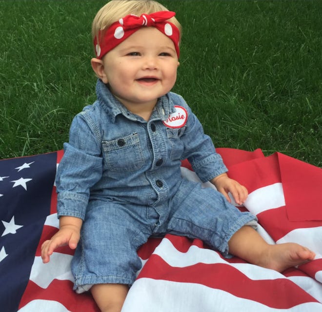 Baby girl sitting on American flag, dressed up as Rosie the Riveter 