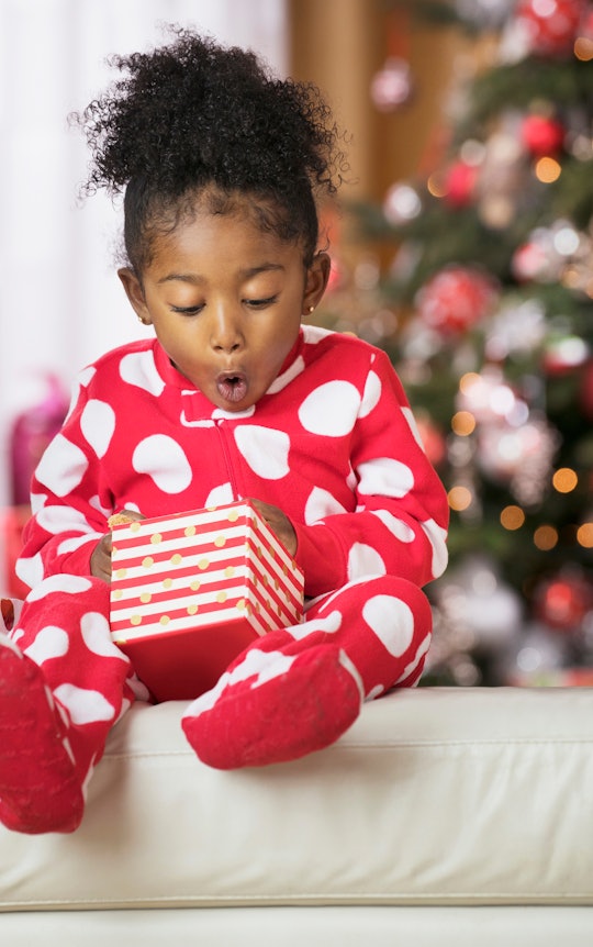surprised and excited young girl in red and while polka dot pajamas opening christmas present