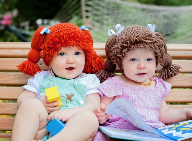 Two babies sitting next to each other wearing wigs that look like Cabbage Patch kids hair