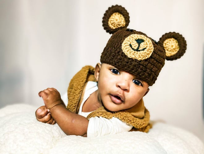 Baby laying on its tummy wearing beanie that looks like teddy bear with ears