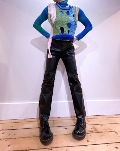 Emma Childs wears a blue turtleneck and multi-colored, cutout vest.