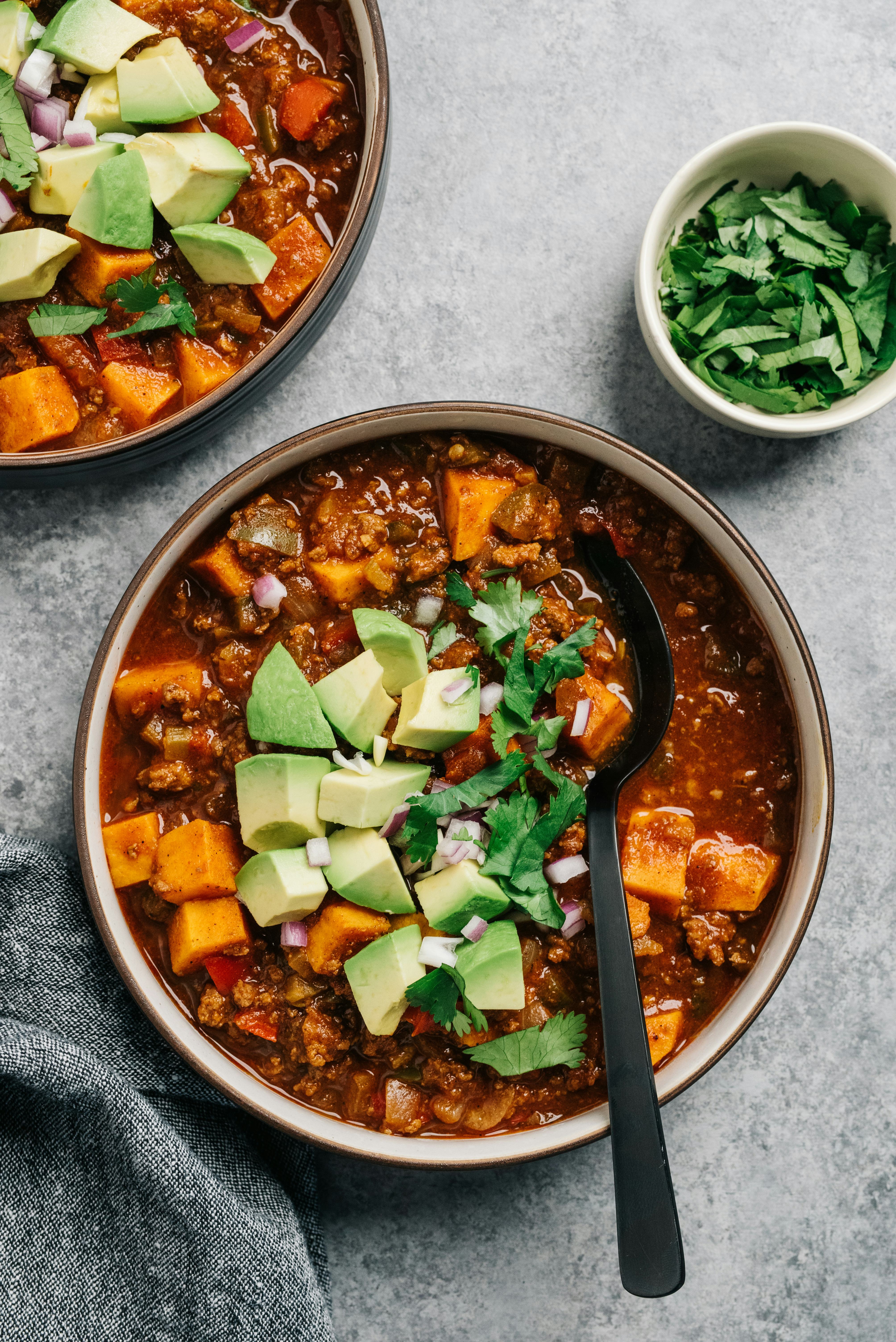 pumpkin chili in a bowl, topped with avocado and herbs
