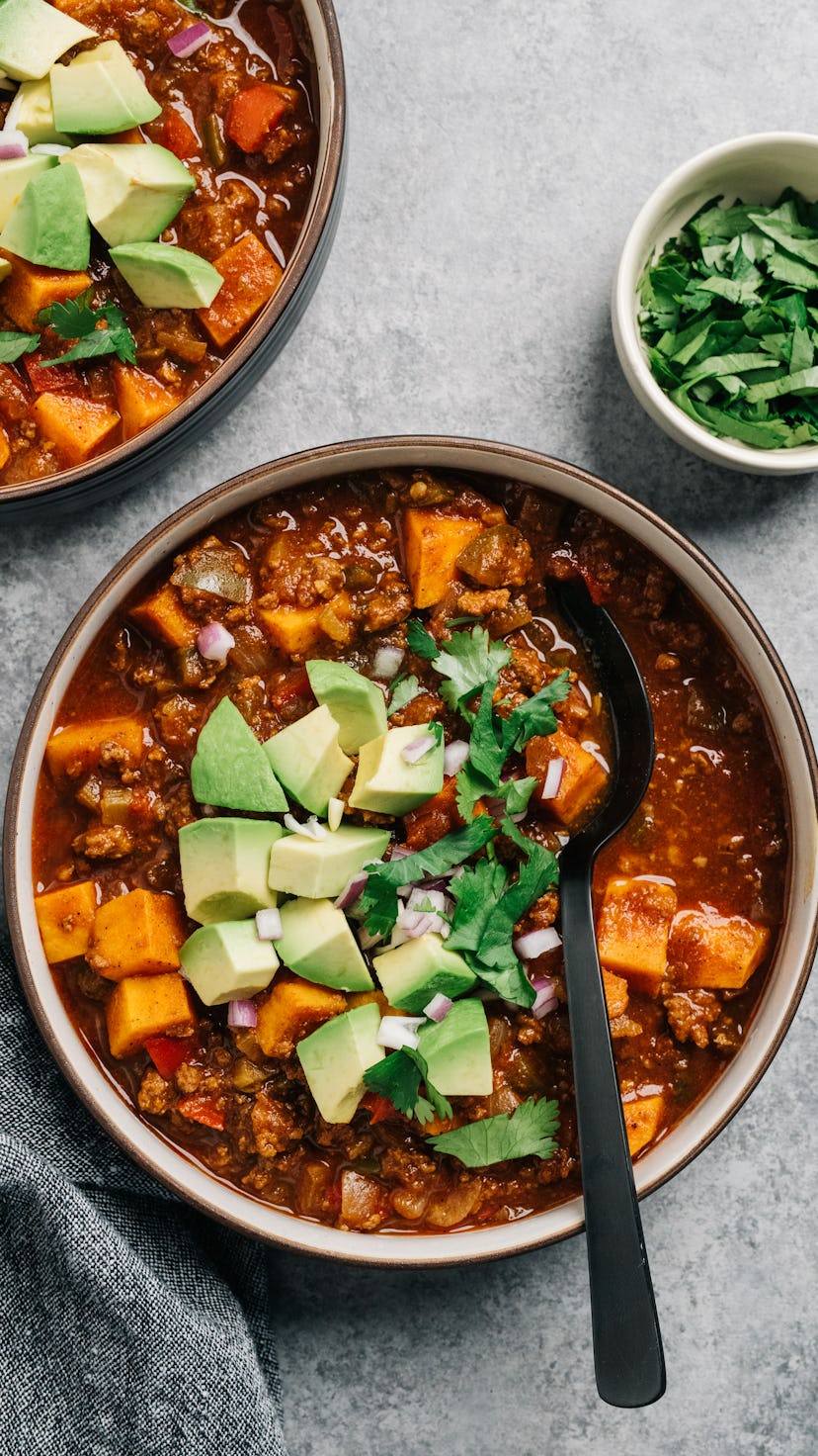 pumpkin chili in a bowl, topped with avocado and herbs