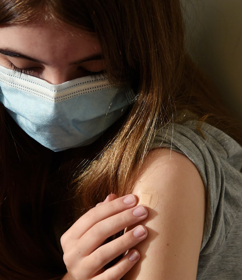 Close up of a young, masked girl holding her shoulder 