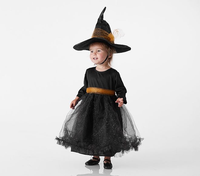 Baby girl standing, wearing a black dress and witch had