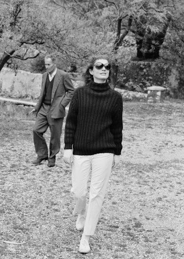 Jackie Kennedy in a black knit sweater, white pants, white sneakers and black sunglasses at the isla...