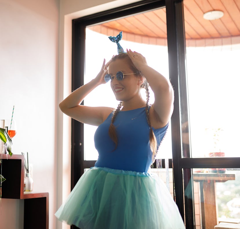 Young woman fixing her mermaid headband on Halloween before posting mermaid costume quotes for Insta...