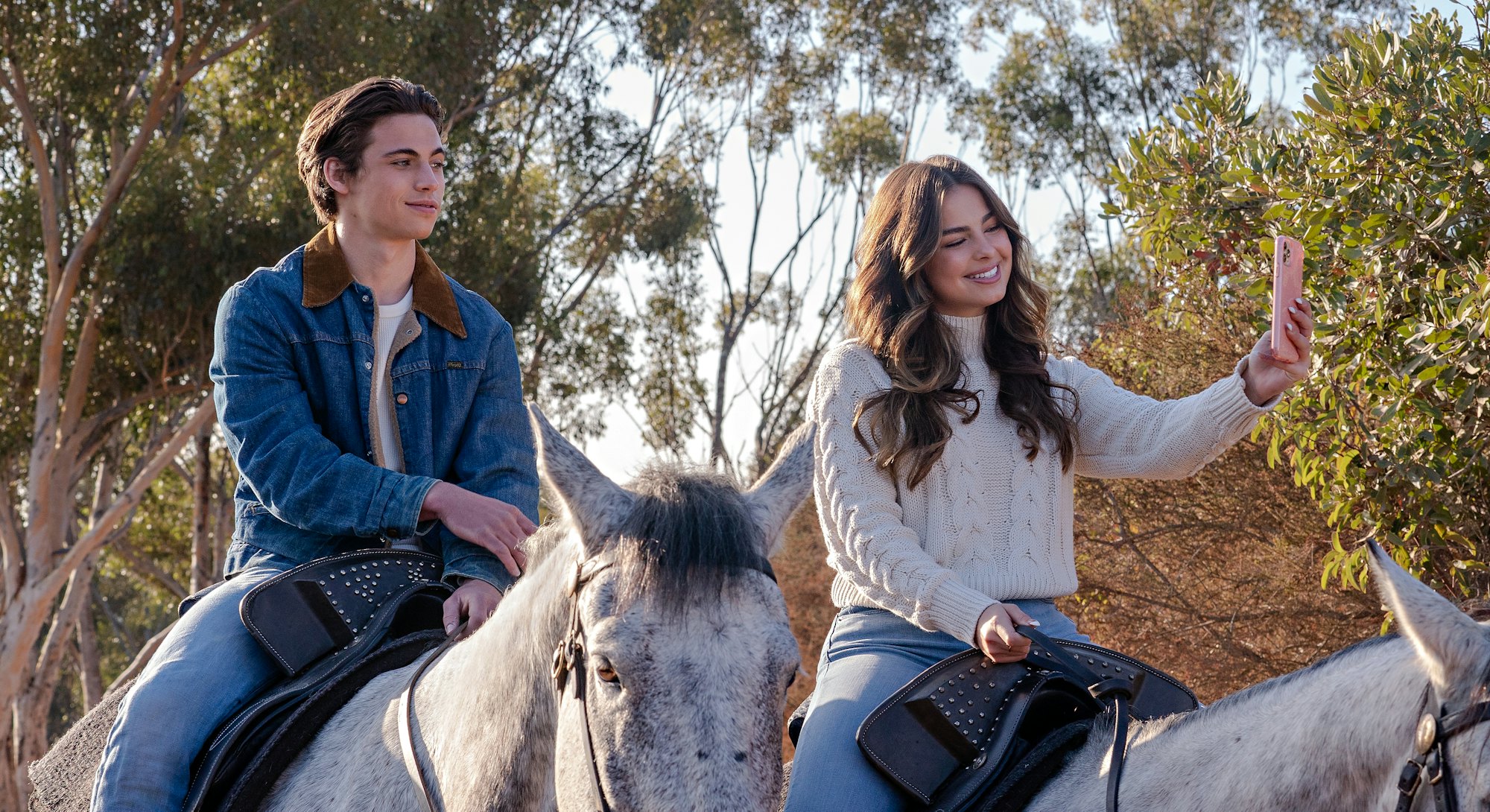 A still from He's All That: main characters Cameron and Padgett ride horses while Padgett snaps a se...