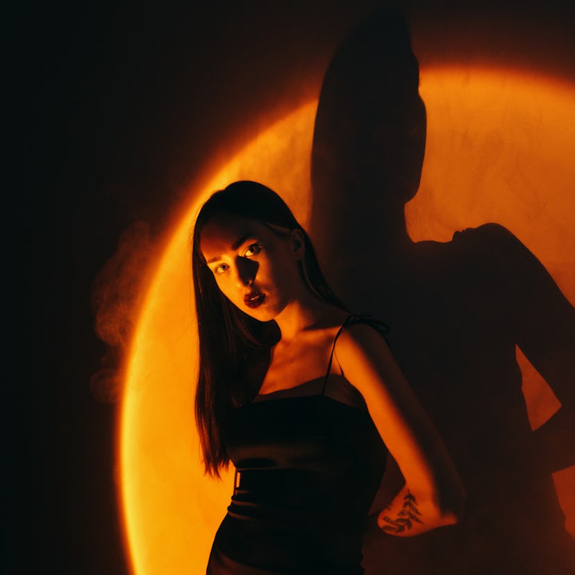 Young woman in black dress standing under the orange light, affected by the September 2021 new moon ...