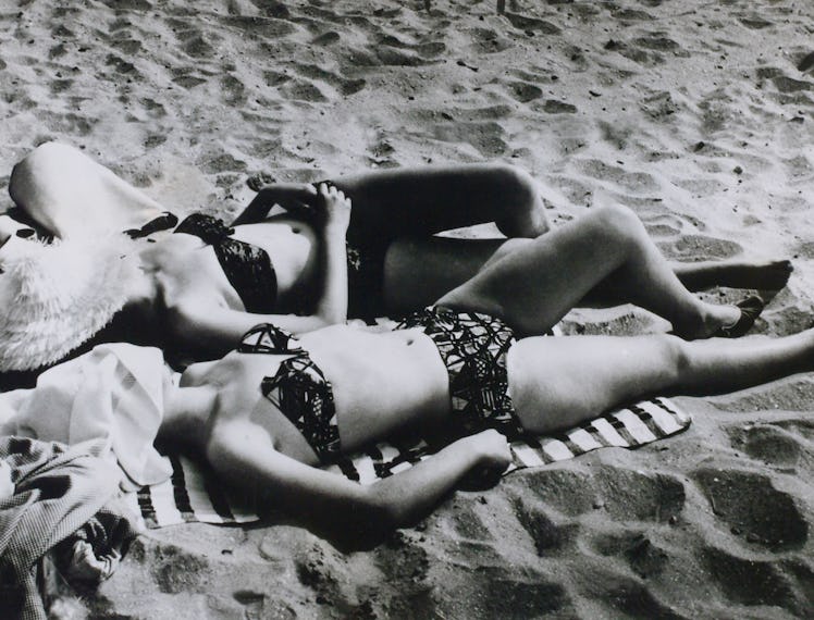 two women wearing hats and bikinis lie on the beach