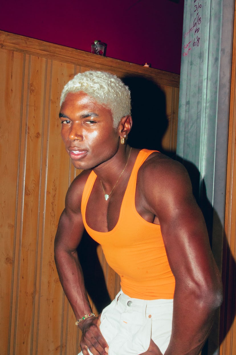 A man with blonde hair in an orange tank top supporting pride month
