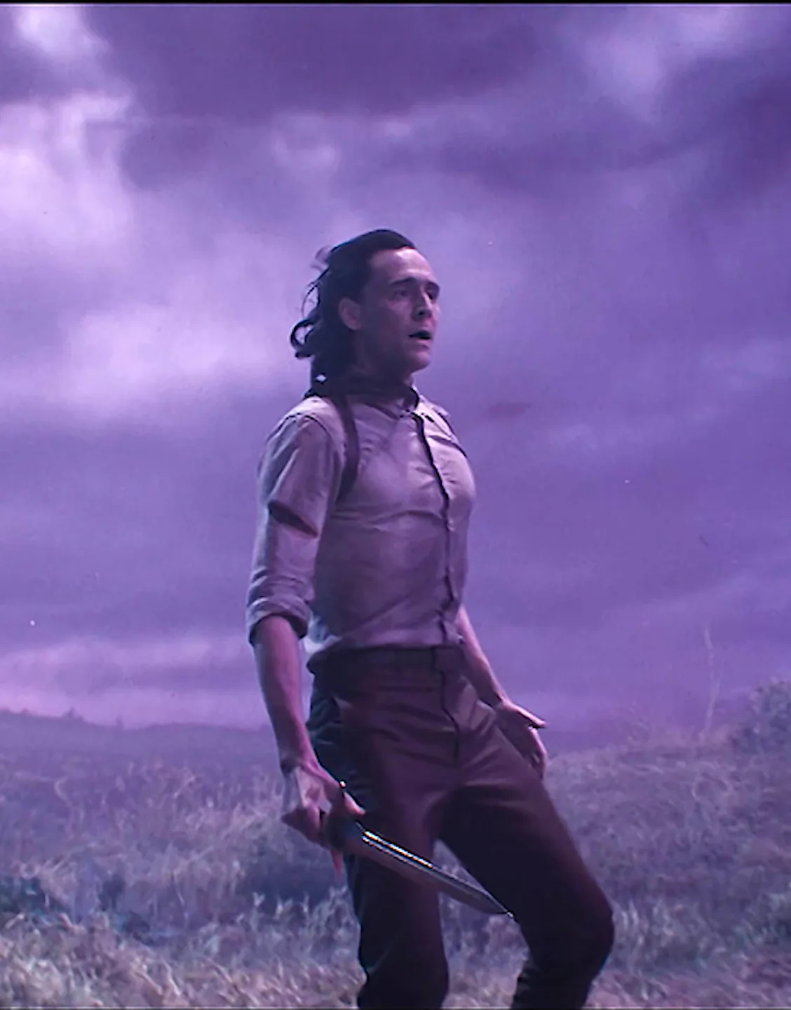 Loki standing on a hill with gloomy clouds above and wind blowing his hair to the back
