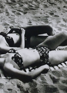 two women in hats and bikinis lie on a beach