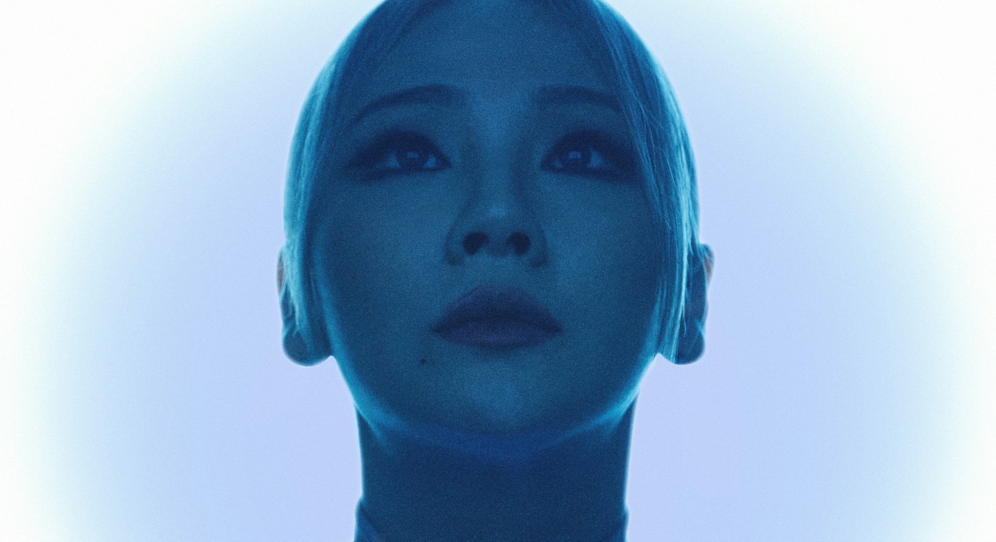CL with a low ponytail, looking up, with a blue light shining over her 