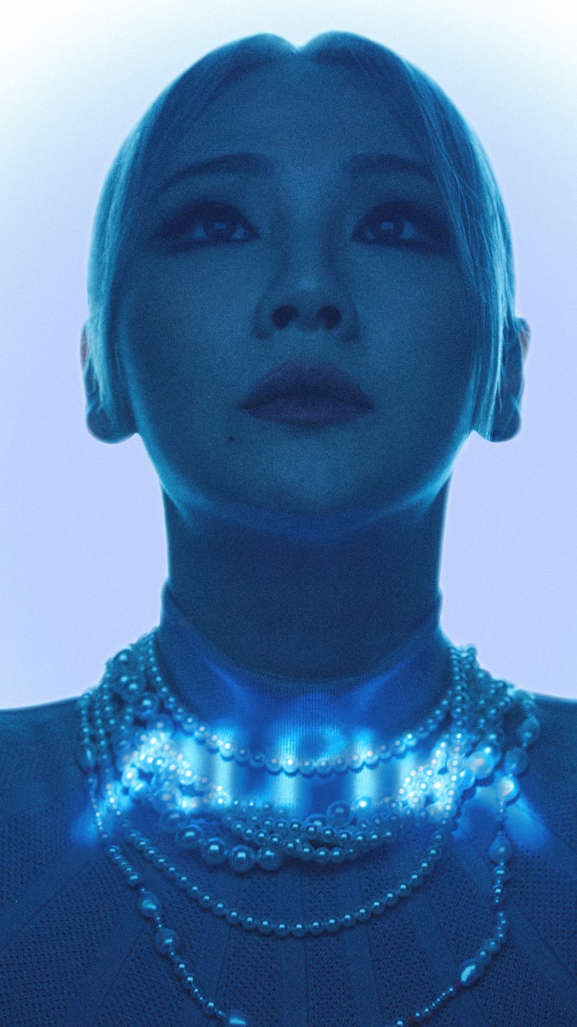 CL with a low ponytail, looking up, with a blue light shining over her 