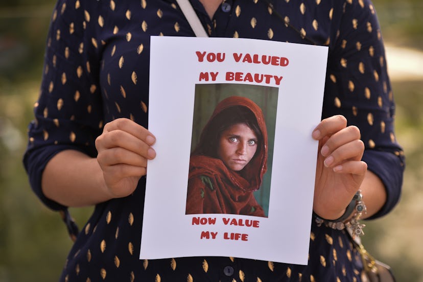 A protester holds the famous Afghan Girl photo, a 1984 photographic portrait of Sharbat Gula by phot...