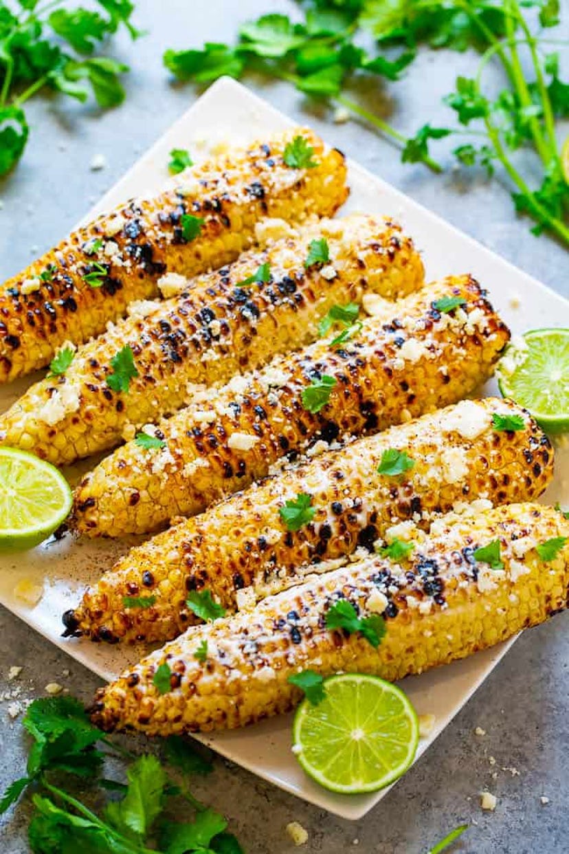 Plate of grilled corn with green garnishes surrounding it