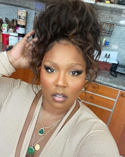 Lizzo with messy bun, winged liner, and beige-and-emerald outfit