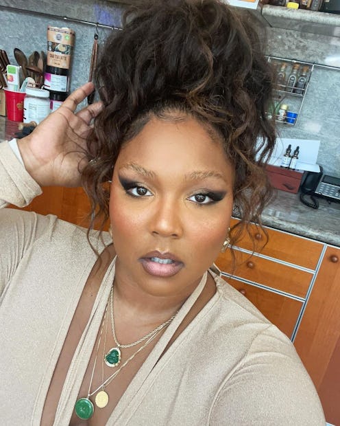 Lizzo with messy bun, winged liner, and beige-and-emerald outfit