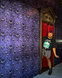 Francis Dominic stands in an Airbnb inspired by Disney's Haunted mansion with Haunted Mansion wallpa...