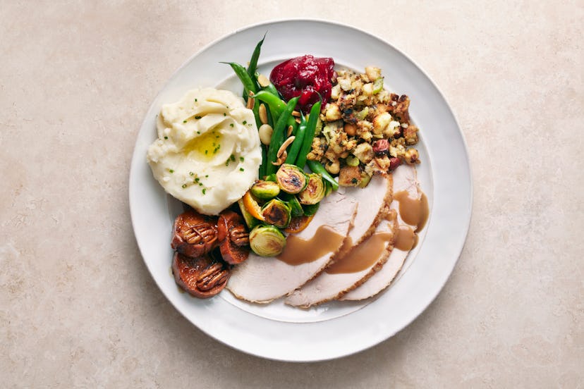 Plate of thanksgiving dinner with turkey, mashed potatoes, brussels sprouts, and more