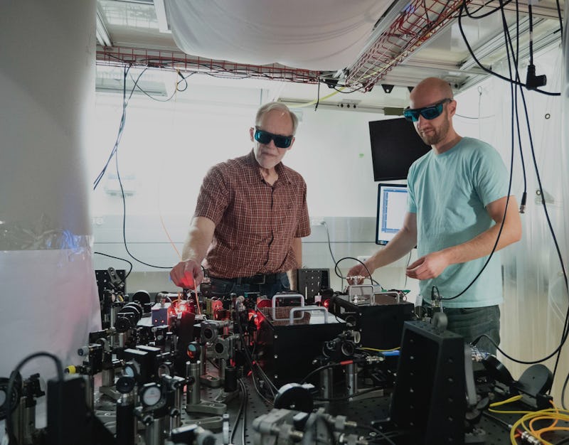 NIST physicists John Bollinger (left) and Matt Affolter adjust the laser and optics array used to tr...