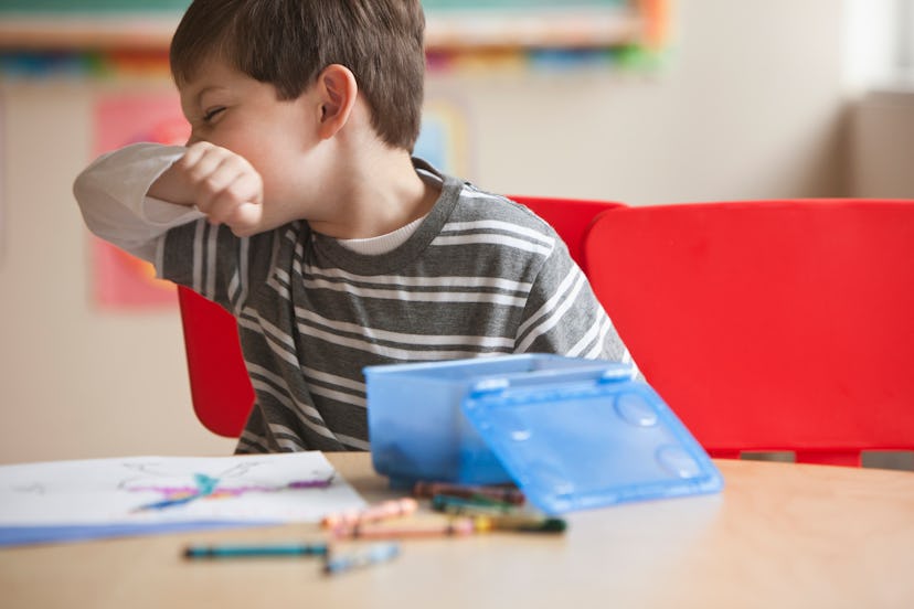 A child at school sneezes into his elbow while drawing with crawyons.