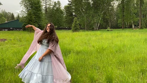 Emma Christensen in a blue dress and pink scarf dancing around a field next to the woods