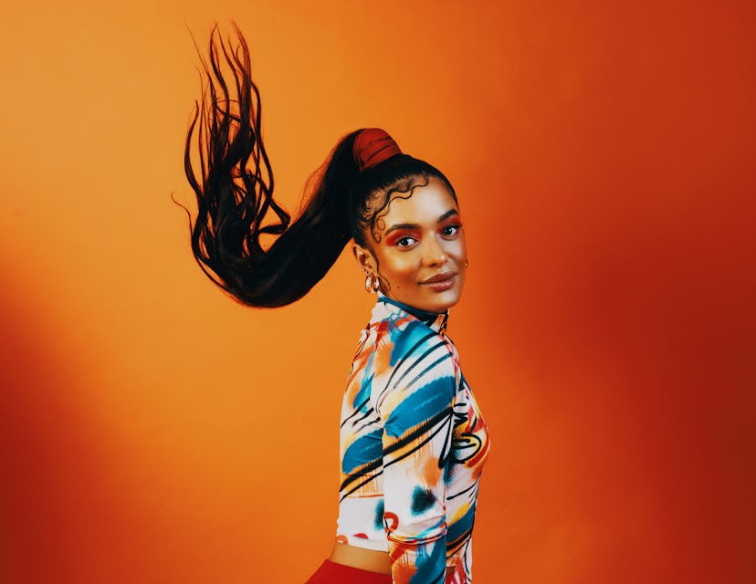 A young Black woman flips her long ponytail and killer makeup, looking ready to go back to school wi...