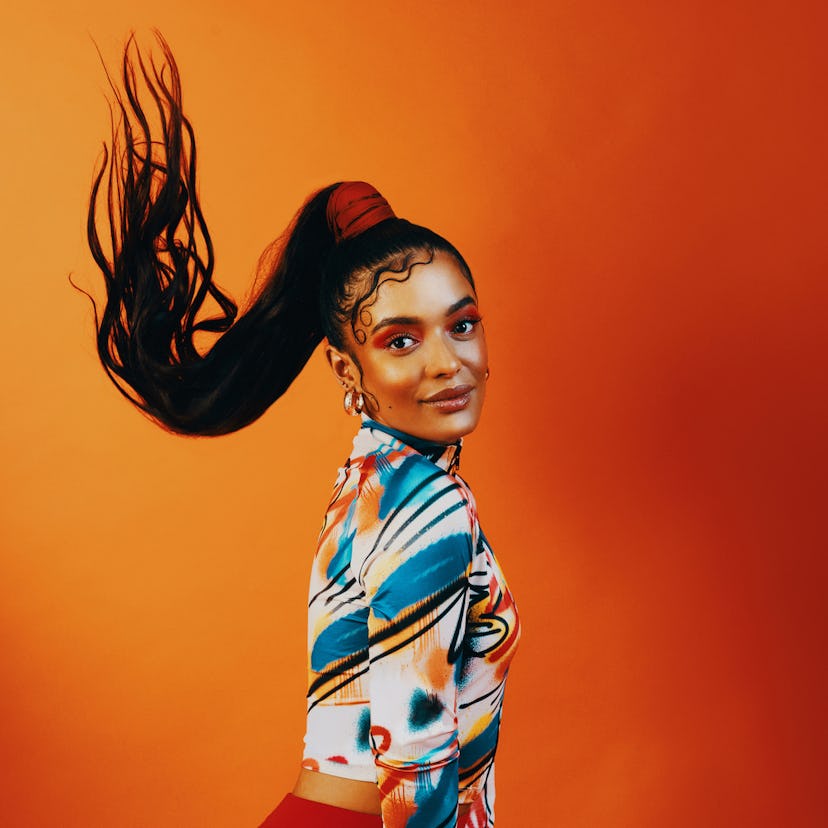 A young Black woman flips her long ponytail and killer makeup, looking ready to go back to school wi...