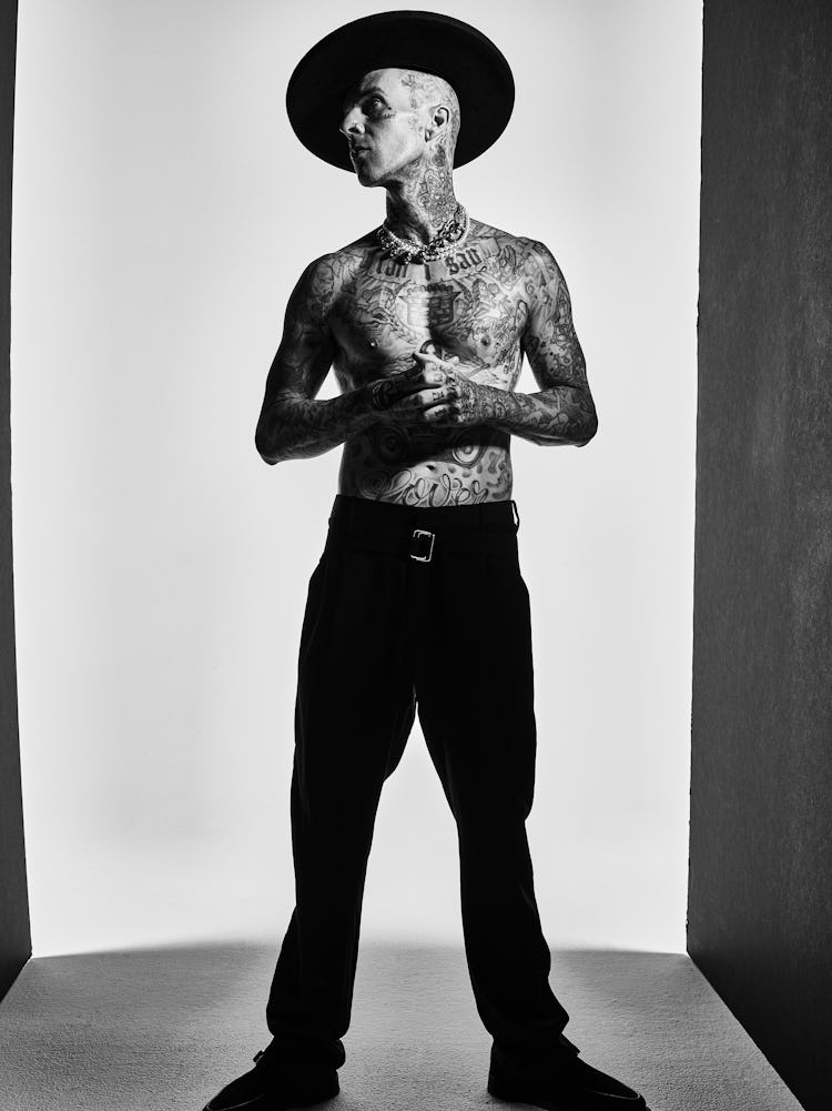 A full-length photo of Travis Barker wearing a wide-brimmed hat shot in black and white.